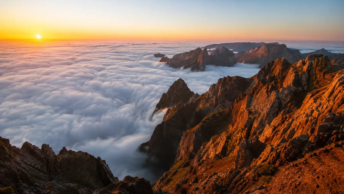 Amanecer sobre un mar de nubes desde el Pico do Areeiro, con las cimas de basalto iluminadas de naranja por encima de las nubes